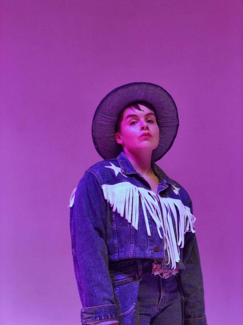 A person in a cowboy outfit posing on a purple background