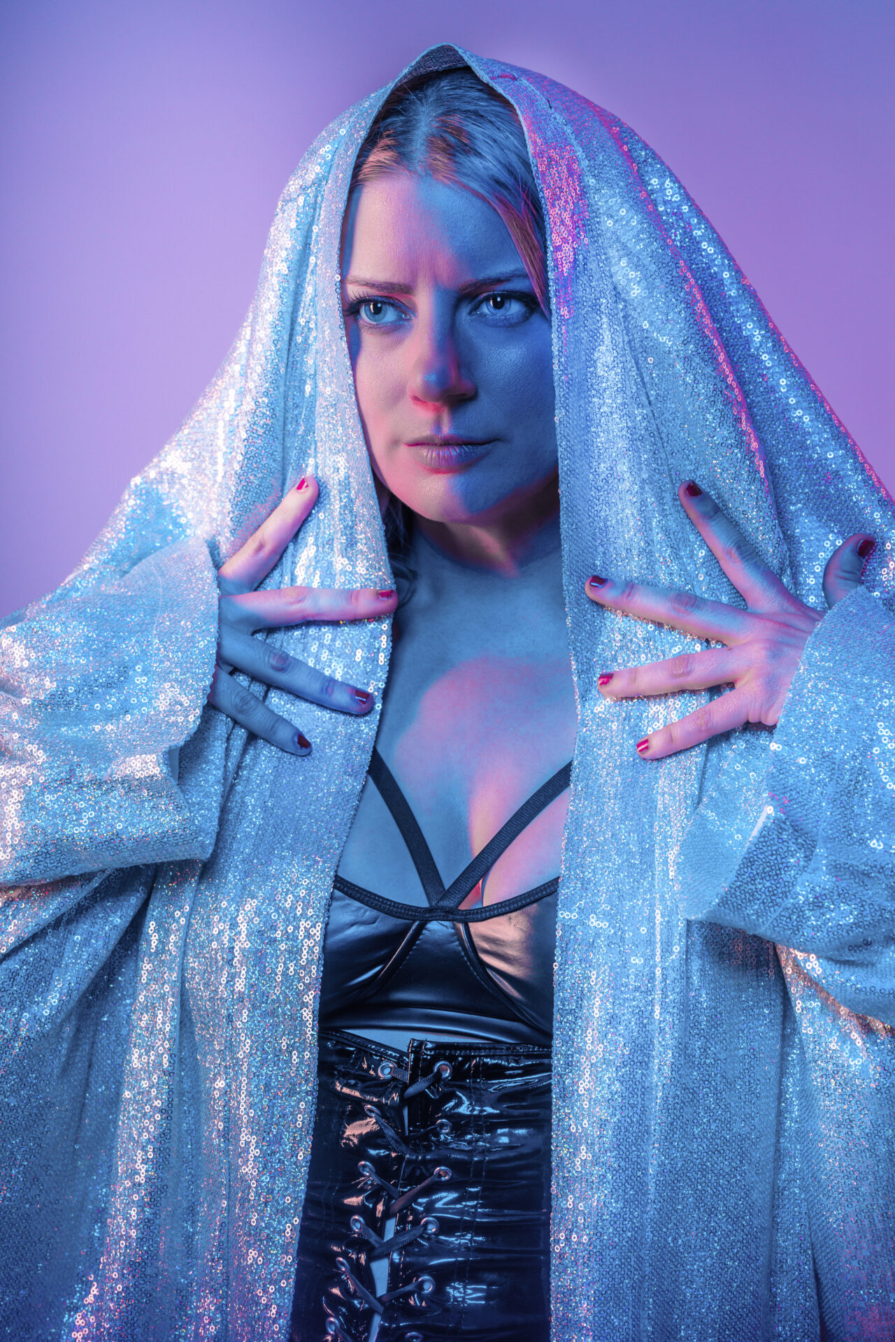 purple and blue blackground with a woman with a stern look on her face holds a sparkly hood over her eyes