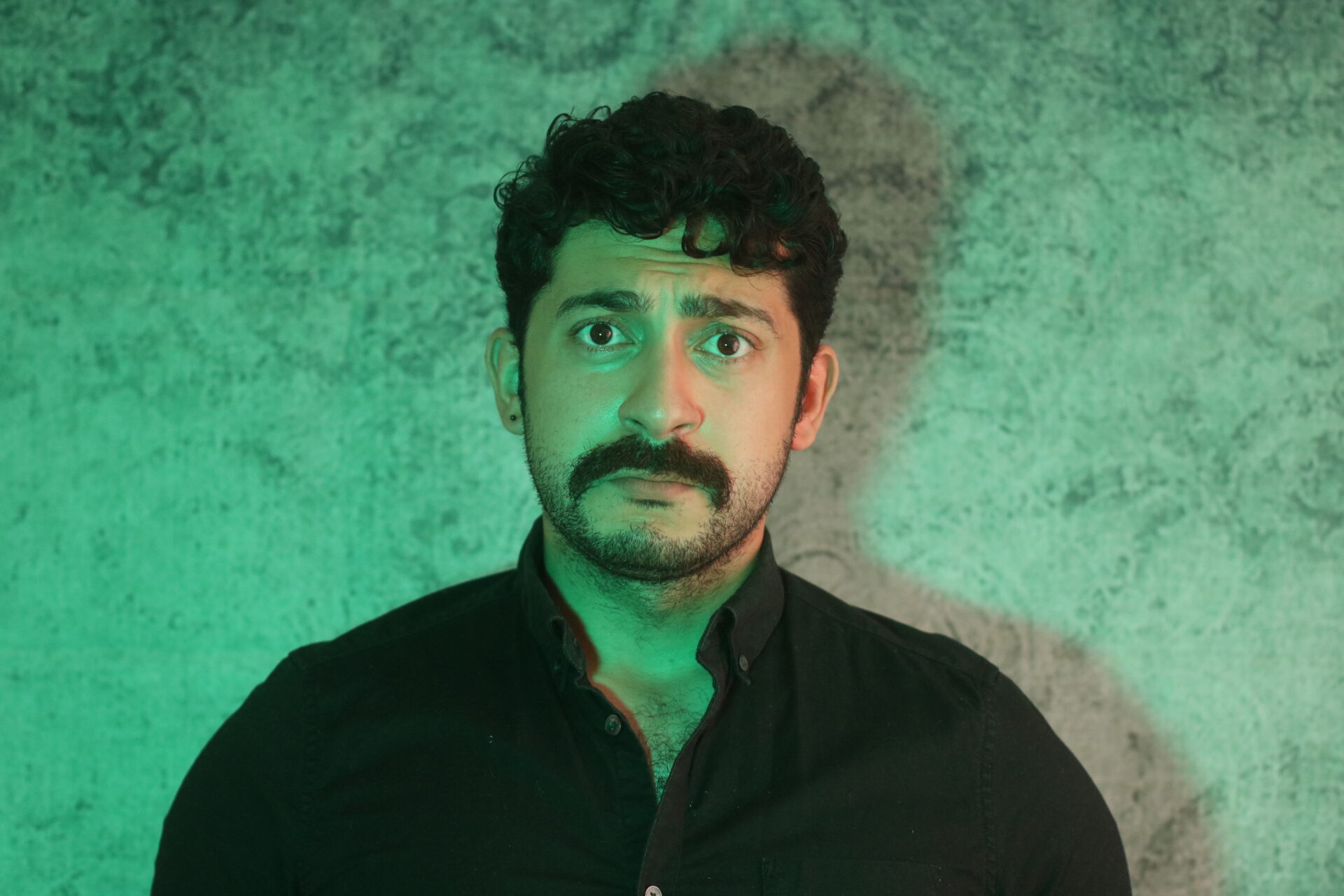 A man in a black shirt with moustache and one earring in their left ear, green hue across the photo.